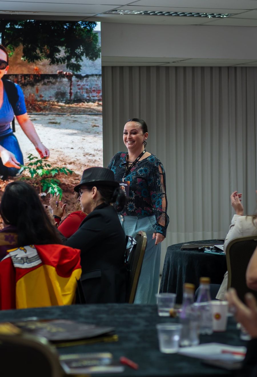 Cynthia M. Cominesi conduzindo um workshop, com participantes sentados em mesas redondas.